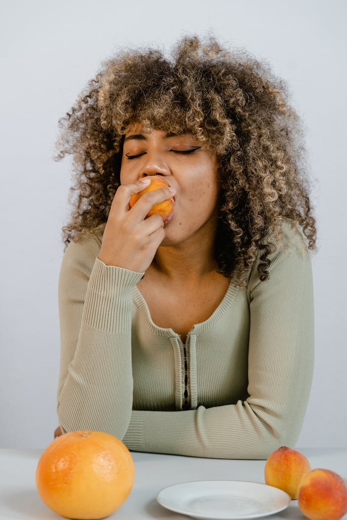 African American woman savoring fresh fruit in a relaxed setting with closed eyes.